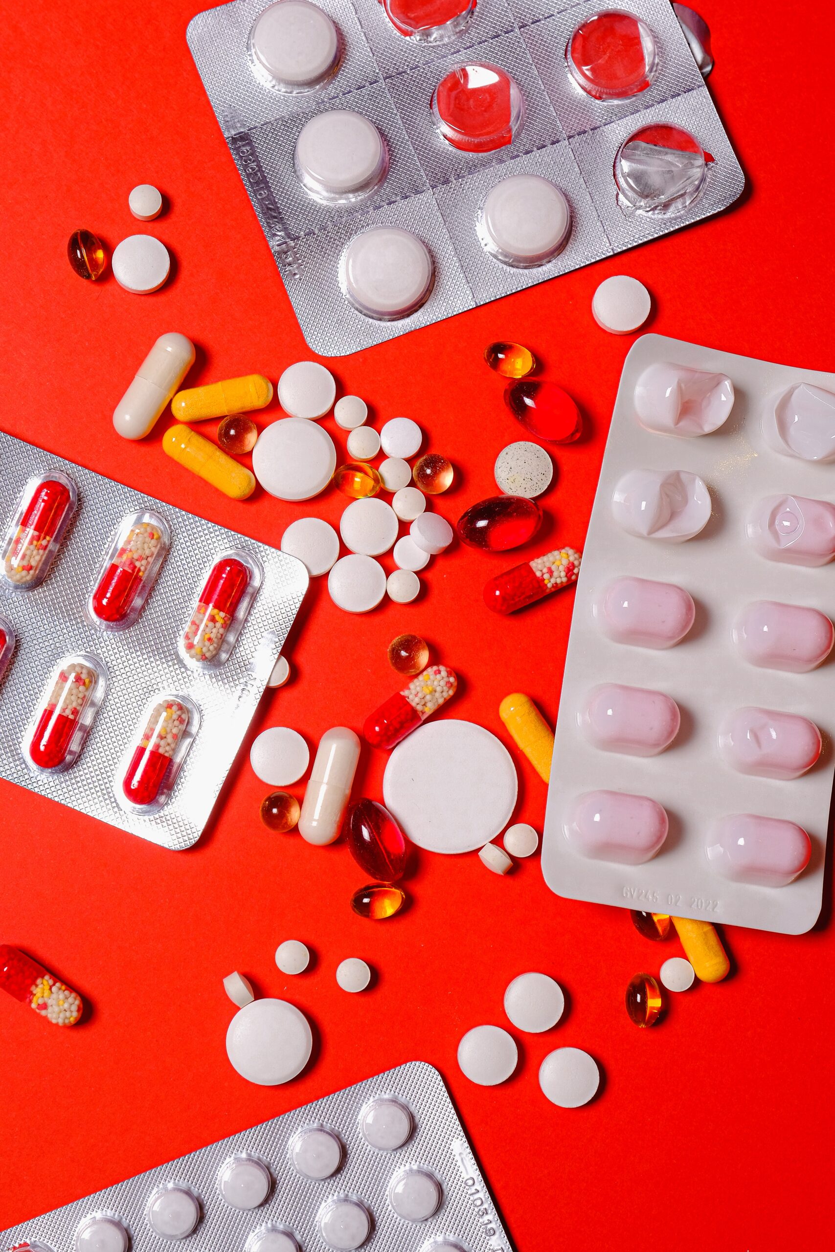 A variety of pills with different shapes and sizes, on a red background.